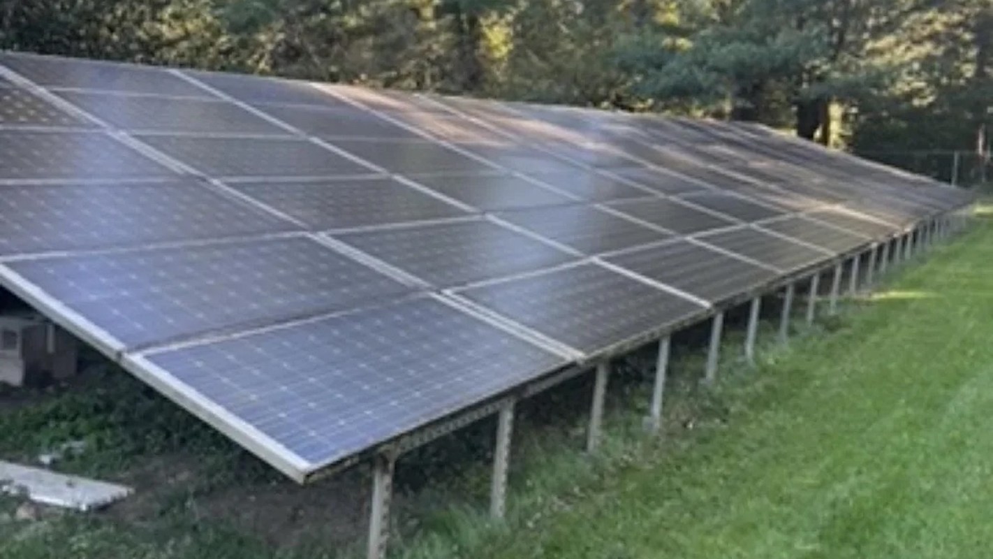 A row of solar panels installed on a grassy area surrounded by trees.