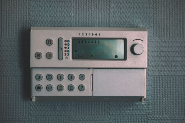 A digital thermostat with a display and various buttons mounted on a textured wall.