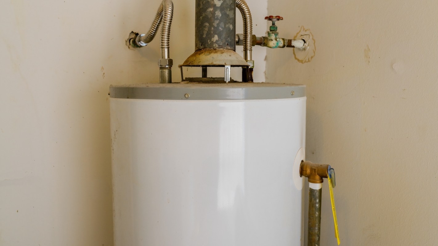 A white water heater with pipes and a valve against a beige wall.