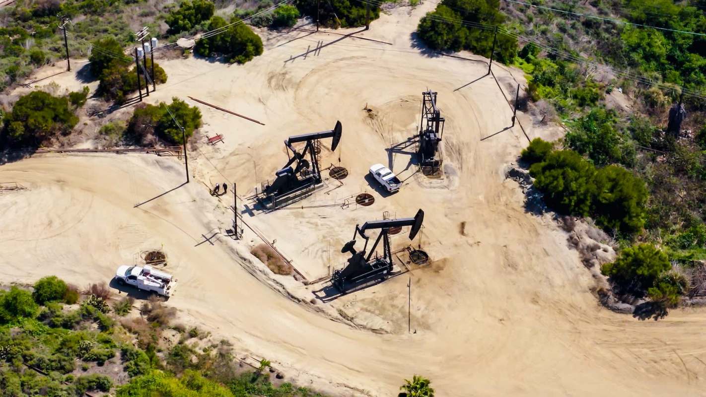 An oil extraction site with several pump jacks, a service truck, and surrounding vegetation.