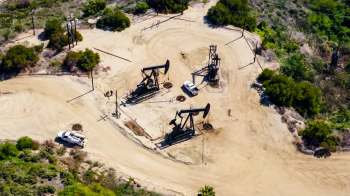 An oil extraction site with several pump jacks, a service truck, and surrounding vegetation.