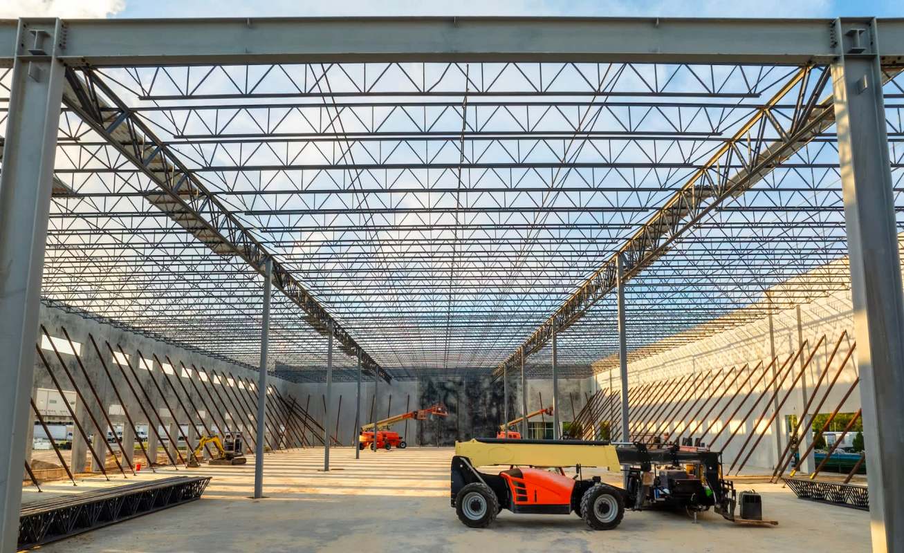 An empty construction site with machinery and a steel frame overhead.