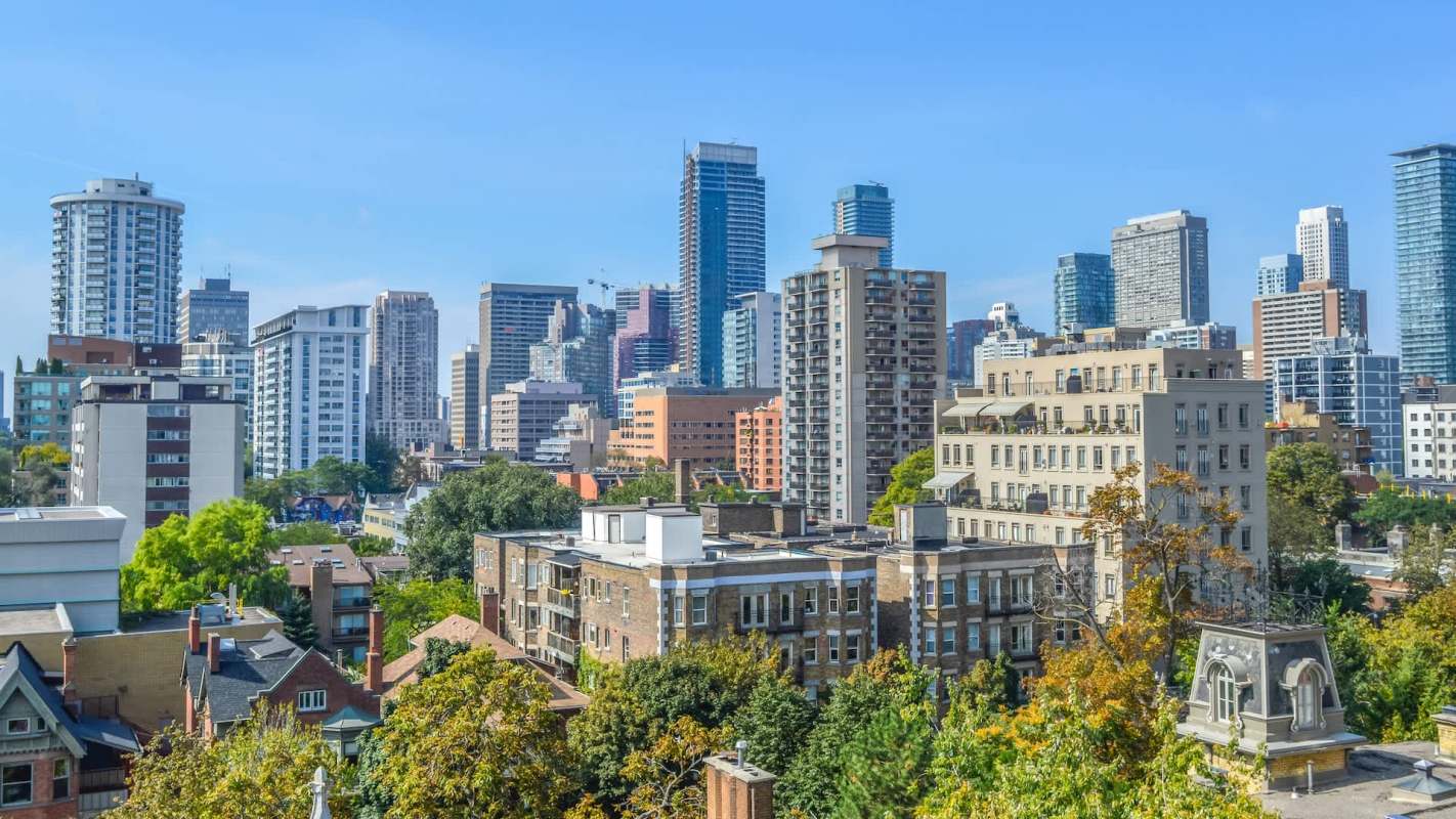 A skyline view of a city featuring a mix of modern skyscrapers and residential buildings amid green trees.
