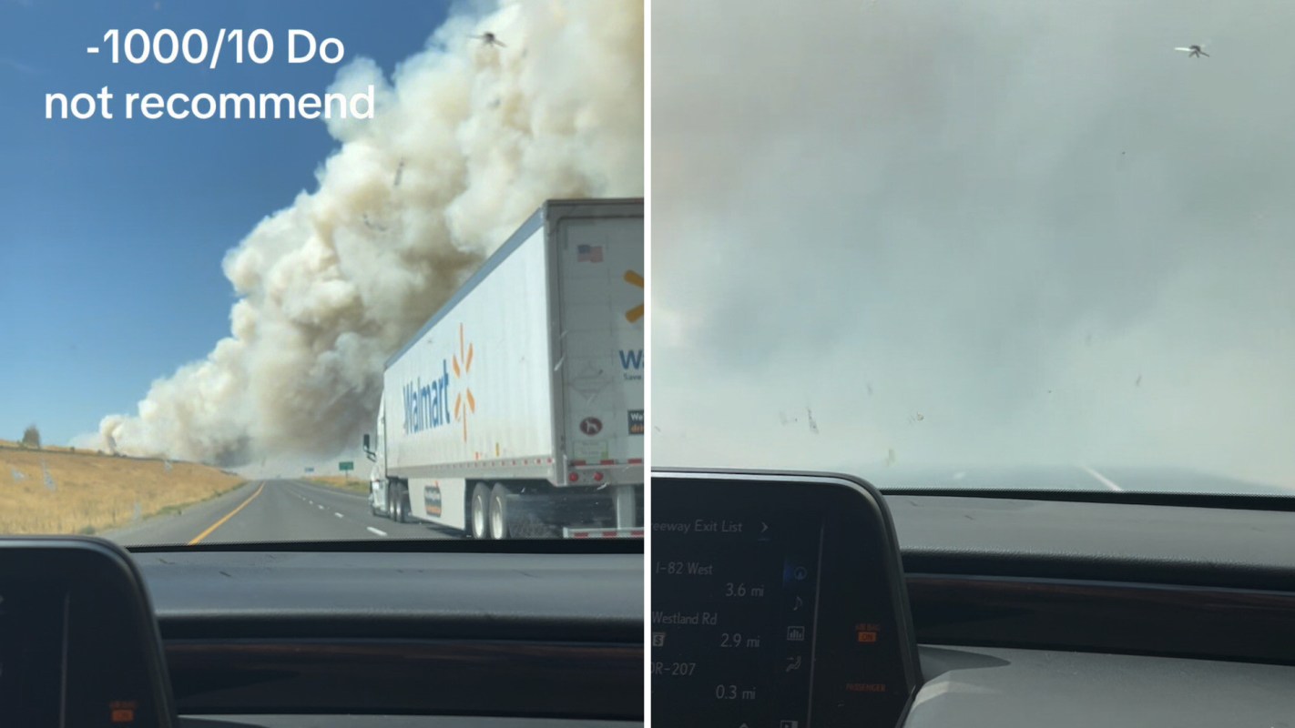 A truck driving on a highway next to a large plume of smoke and a view of limited visibility ahead.