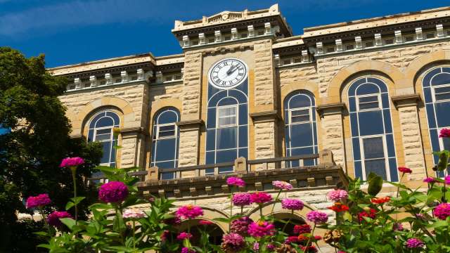 A building with a clock tower and large windows, surrounded by colorful flowers.