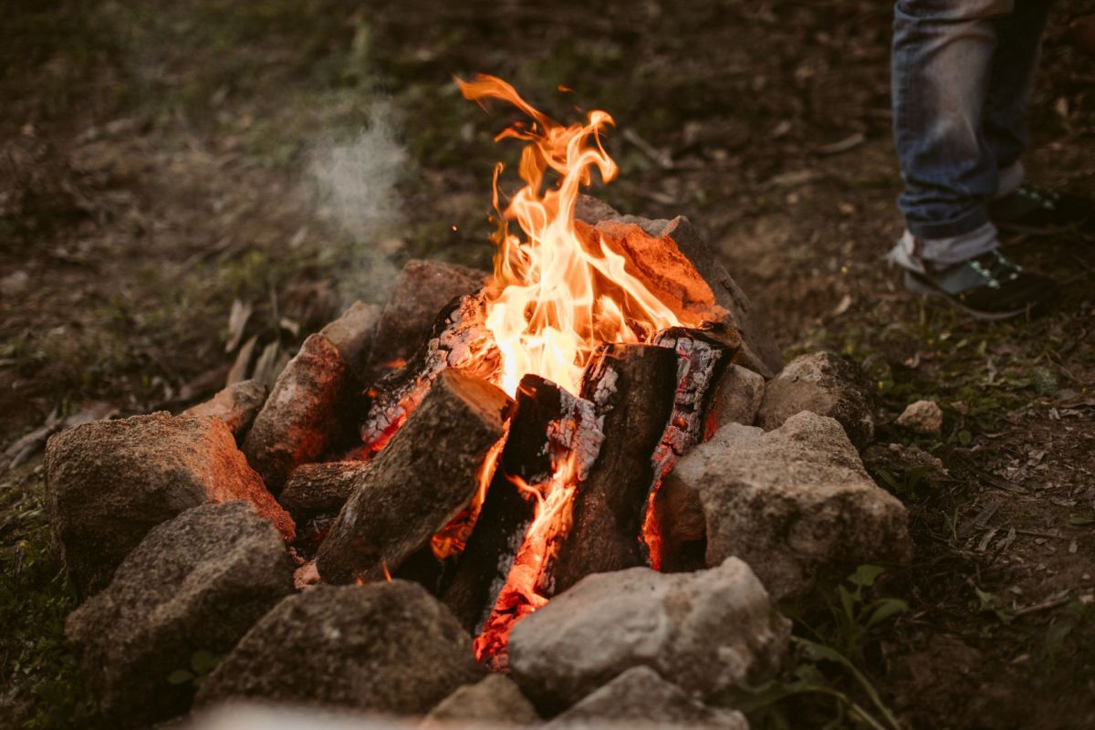 A small fire with wood surrounded by rocks burns with a person's leg nearby