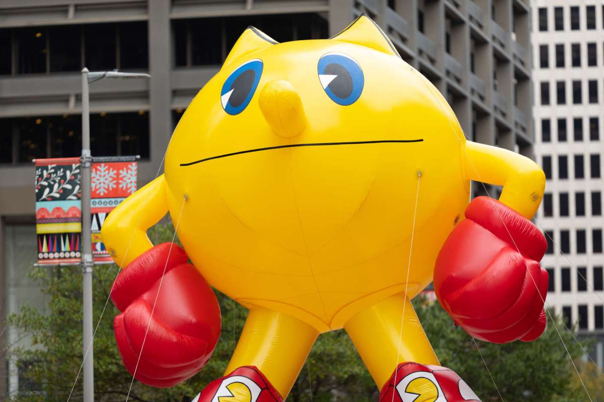 A large inflatable yellow character with red gloves and shoes stands in an urban setting.