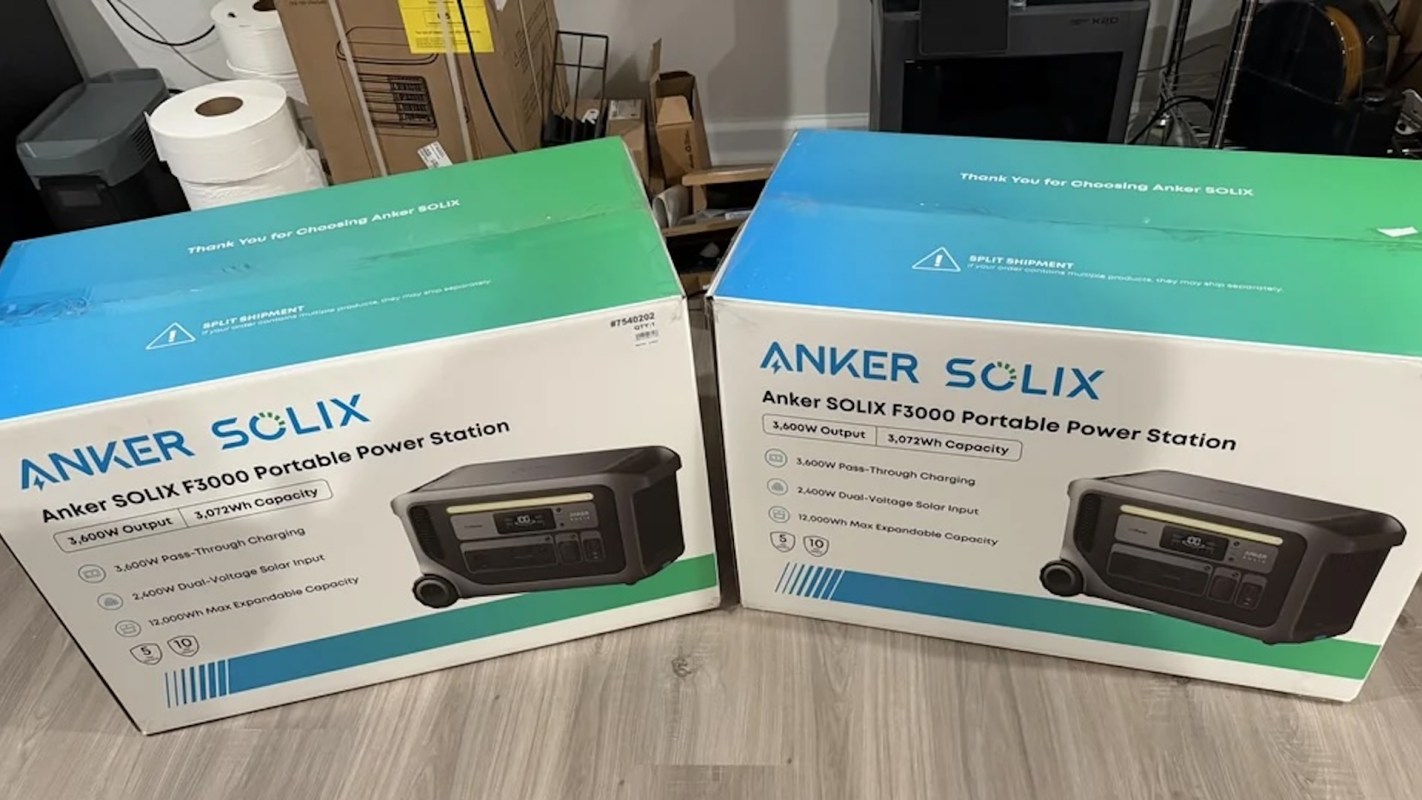 Two Anker SOLIX F3000 portable power station boxes on a floor with additional household items in the background.