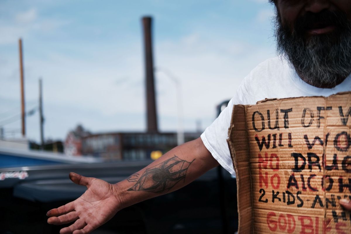 A man with an outstretched arm holds a cardboard sign