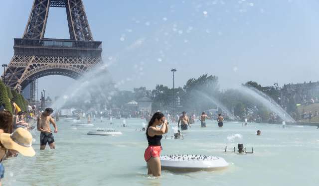 People in a large water basin with fountains, set against the backdrop of the Eiffel Tower.
