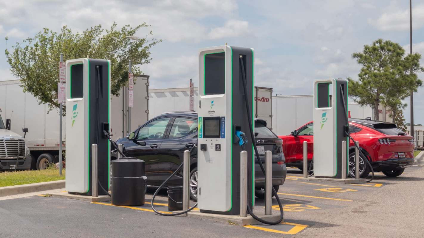 Two electric vehicle charging stations are available in a parking lot next to parked cars.
