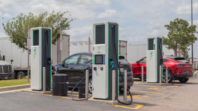 Two electric vehicle charging stations are available in a parking lot next to parked cars.