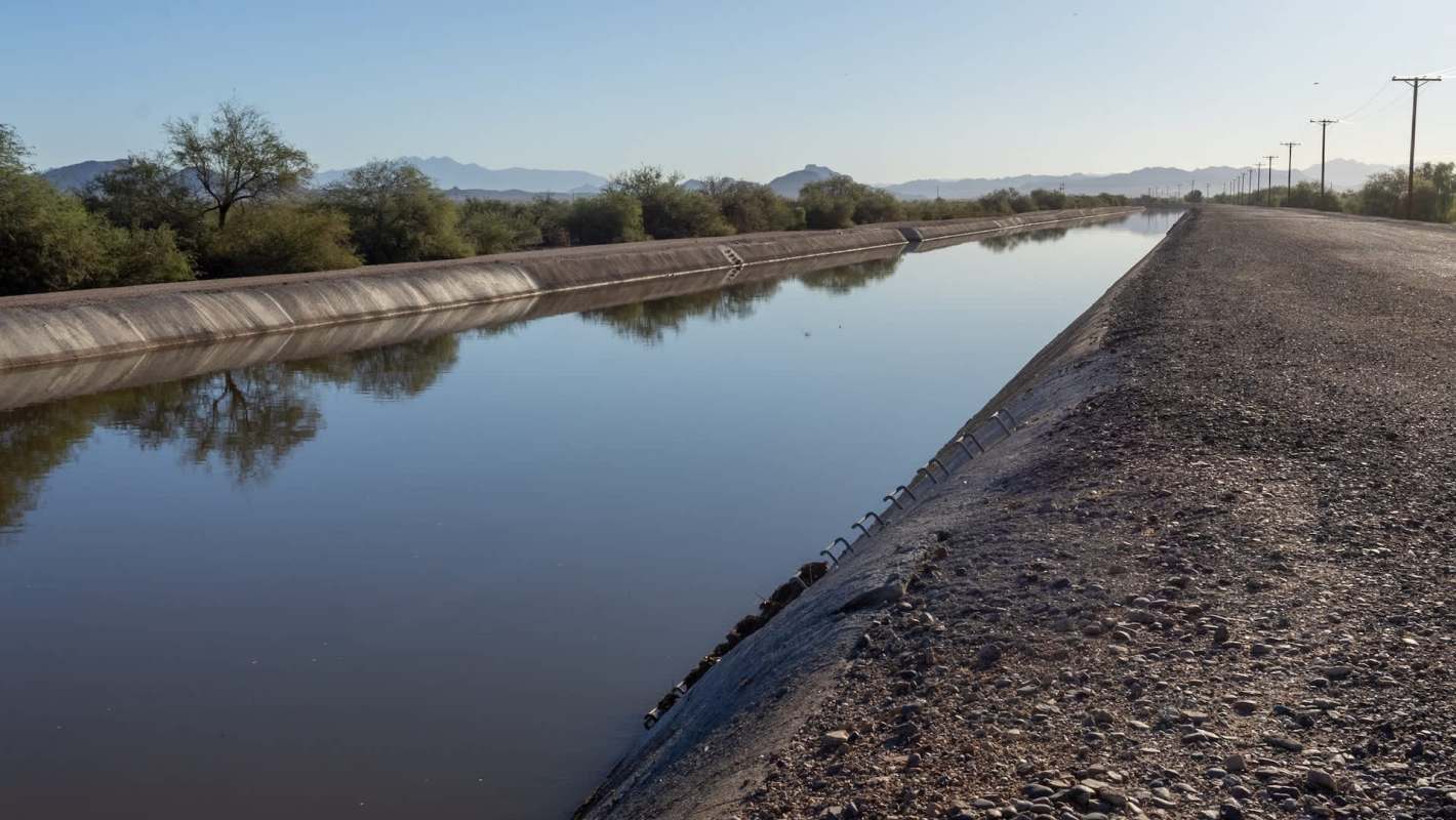 A water canal lined with rocky edges and vegetation under clear blue skies.