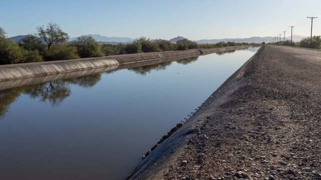 A water canal lined with rocky edges and vegetation under clear blue skies.