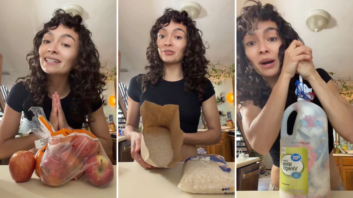A person stands behind a table with apples, rice in a bag, and a bottle of vinegar while trying to stuff plastic into it.