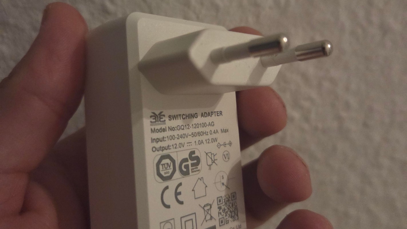 A hand holding a white switching adapter with specifications printed on the side.