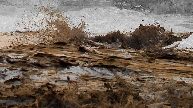 Mud and water splashing violently, creating waves and foam in a turbulent scene.