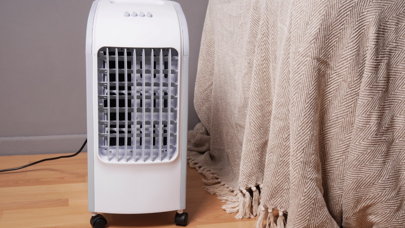A portable fan next to a beige blanket.