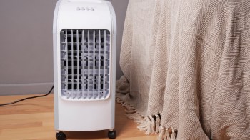 A portable fan next to a beige blanket.