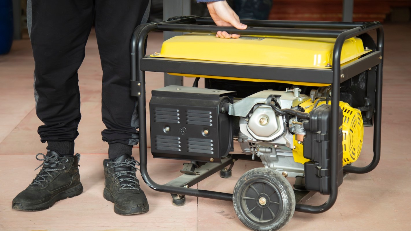 A person is holding the handle of a yellow and black portable generator.