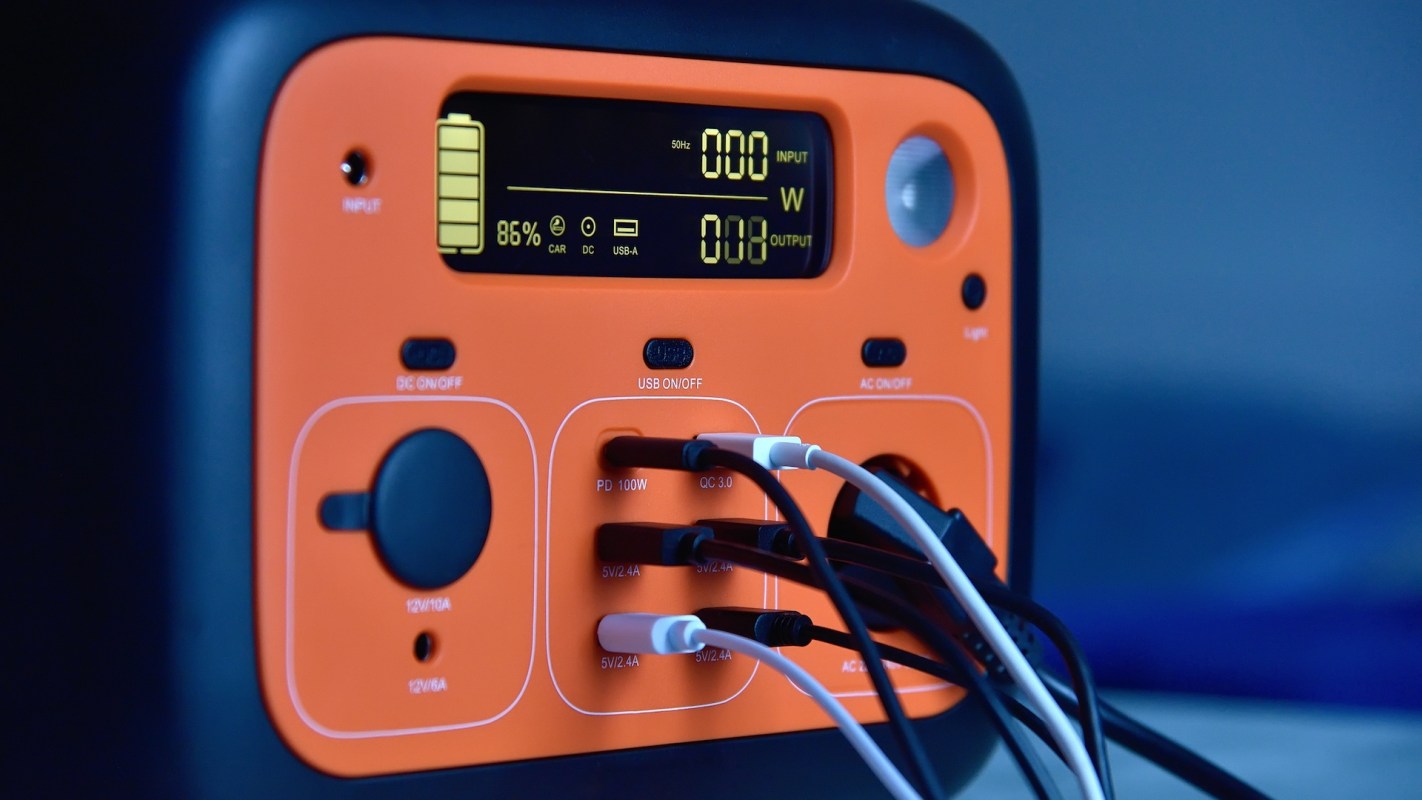 An orange power station with various input and output ports, displaying a battery percentage and power output.