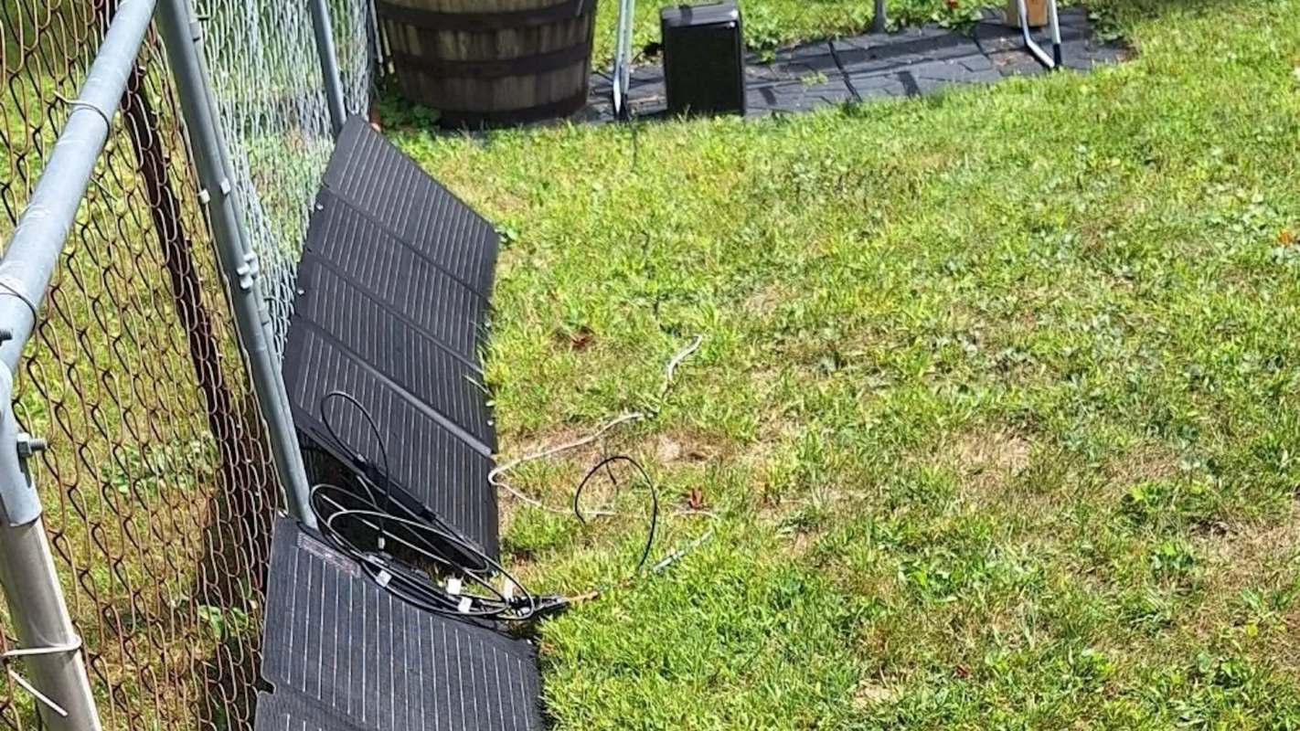 A section of grass with a fence, solar panel, and scattered cables.