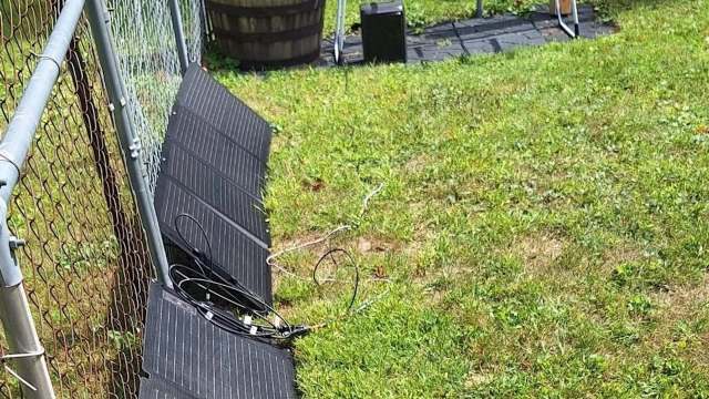 A section of grass with a fence, solar panel, and scattered cables.