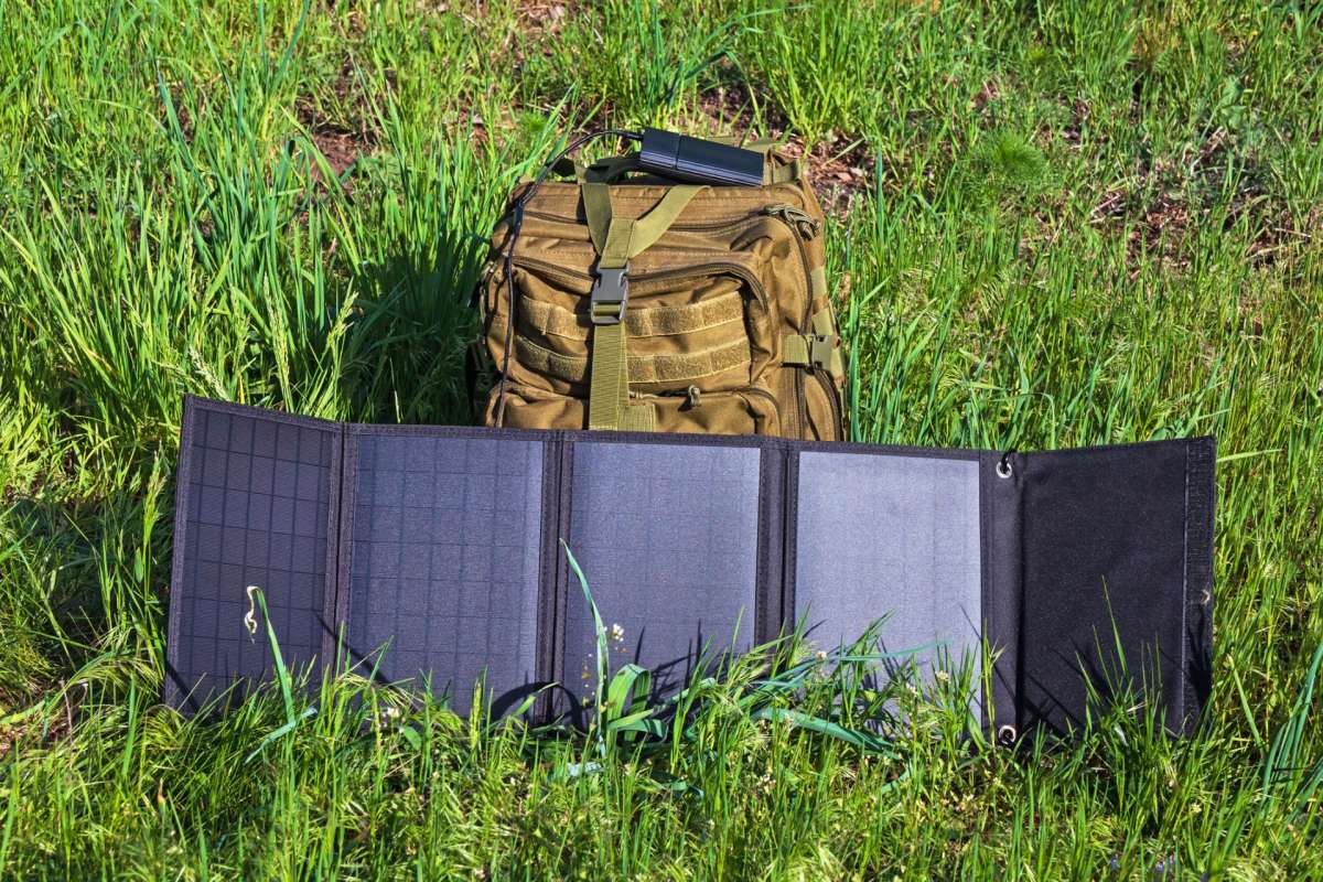 A solar panel is displayed on grass next to a military-style backpack.