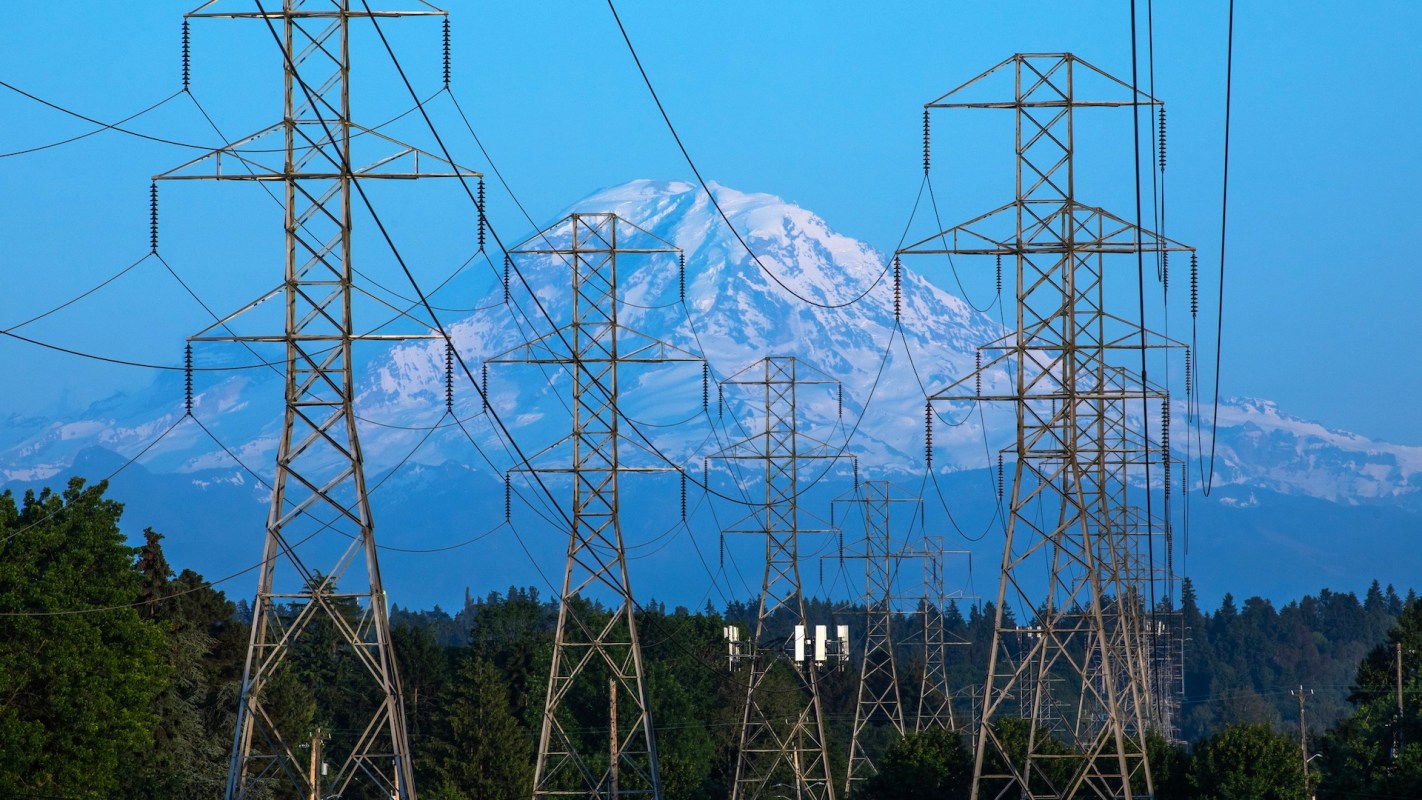 Power lines and towers in the foreground with a snow-capped mountain in the background.
