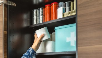 A hand reaches for a roll of paper towels on a shelf with various containers and canned goods.