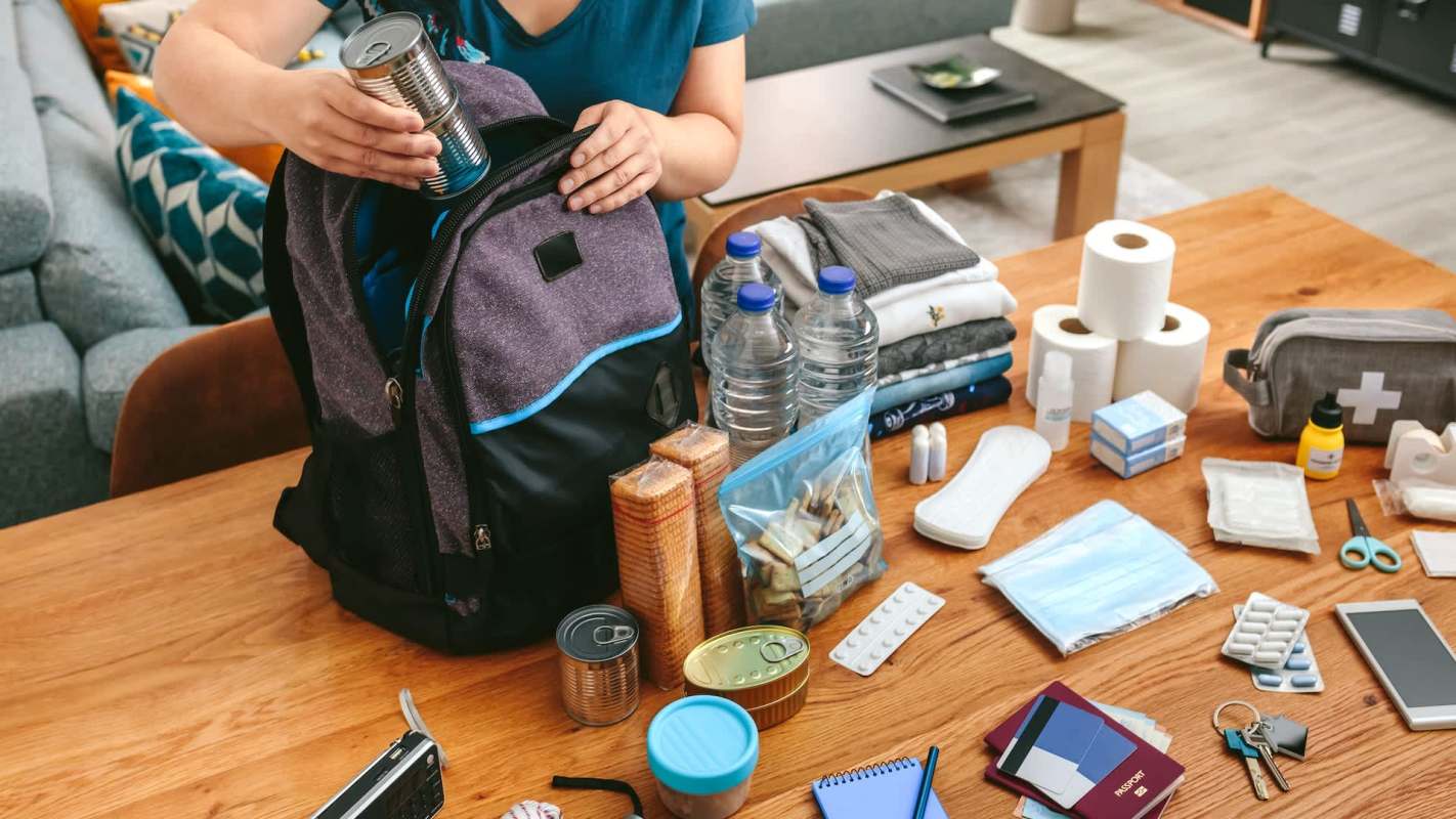 A person packing emergency supplies in a backpack.