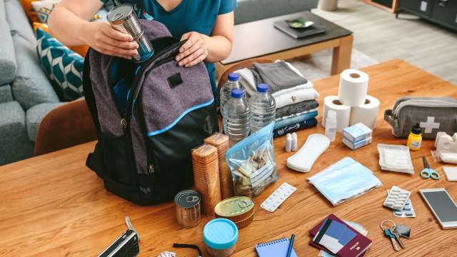 A person packing emergency supplies in a backpack.