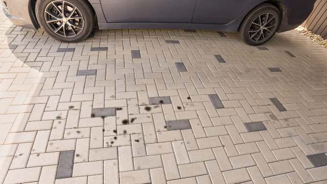 Oil stains on a patterned paved surface beside a parked car.