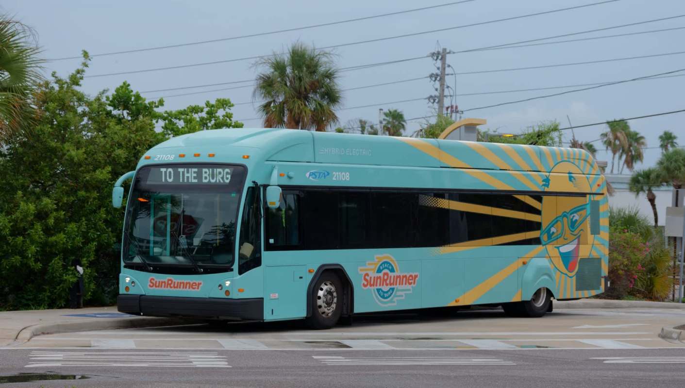 A hybrid electric bus with a colorful design, displaying "TO THE BURG" on its front sign.
