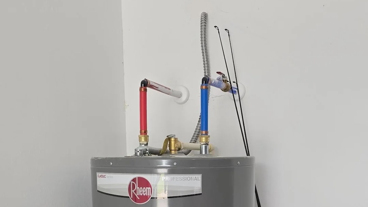 A water heater with red and blue pipes connected to the top.