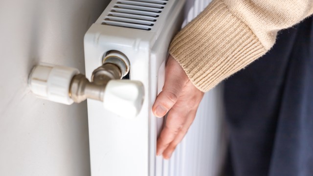 A hand touches a white radiator attached to the wall.