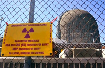 A caution sign indicating a radiologically controlled area near a large industrial structure.