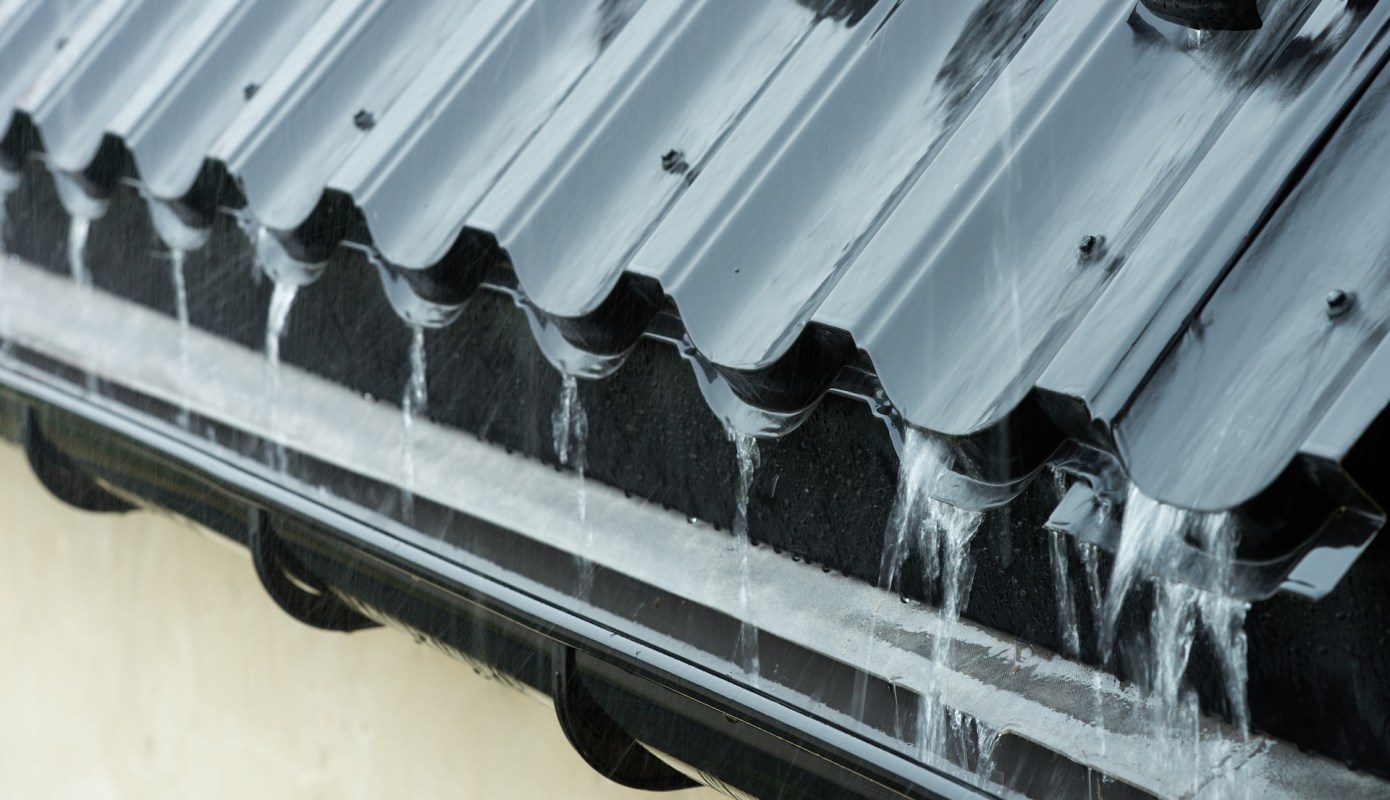 Water flows from a black metal roof into a drainage gutter.