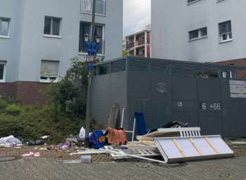 A pile of discarded furniture and debris next to a gray storage unit by a building.