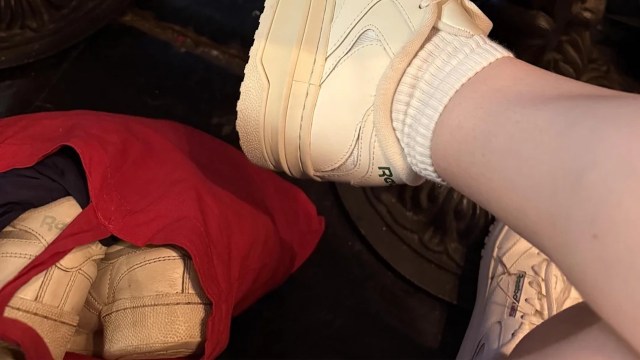 A white sneaker rests near a red bag containing another pair of sneakers.