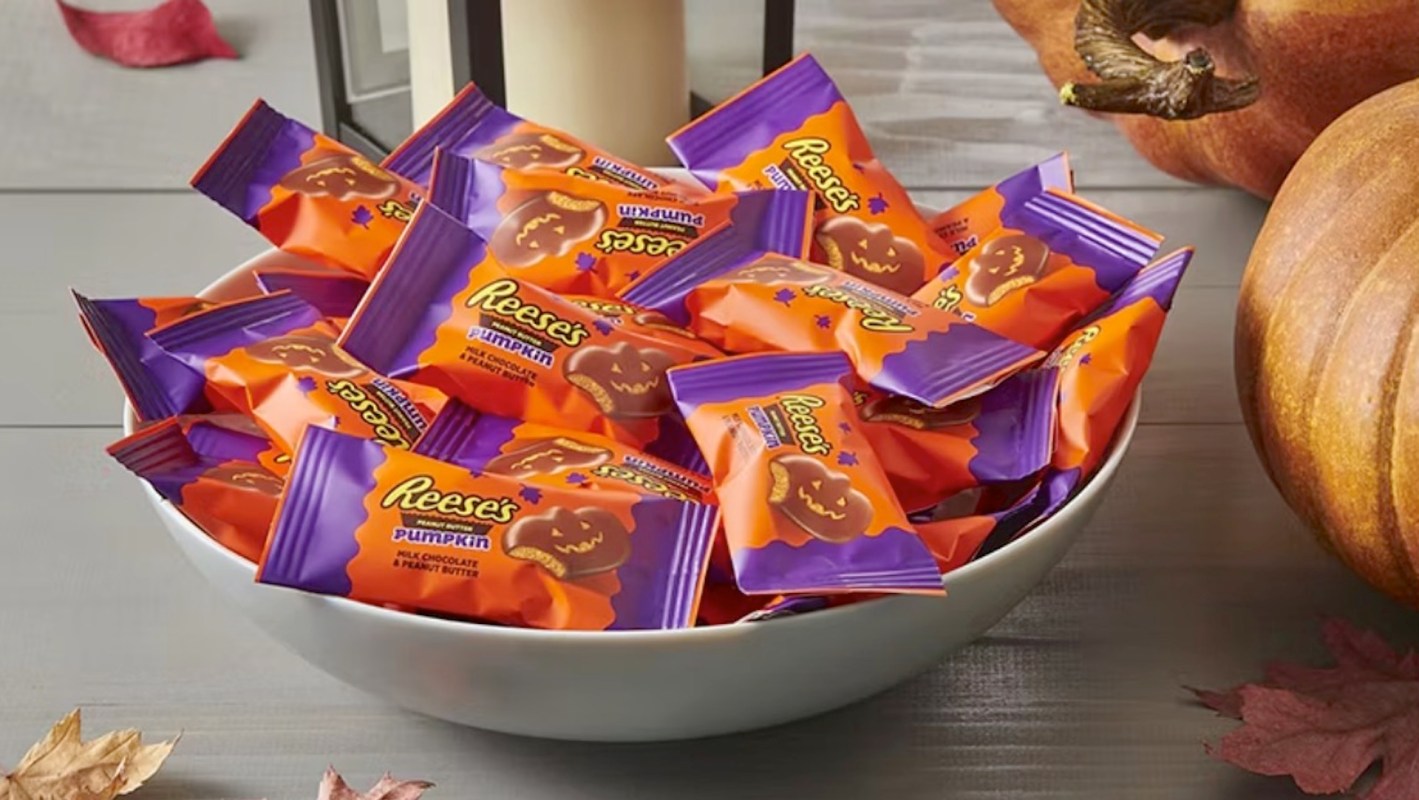 A bowl filled with Reese's pumpkin-shaped candies, surrounded by pumpkins and autumn leaves.
