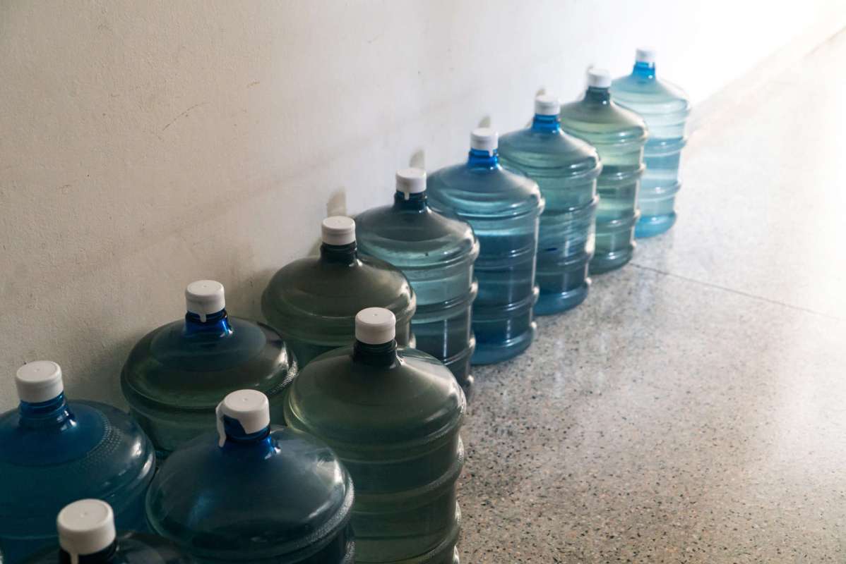 A row of large water bottles in various shades of blue and green against a wall.