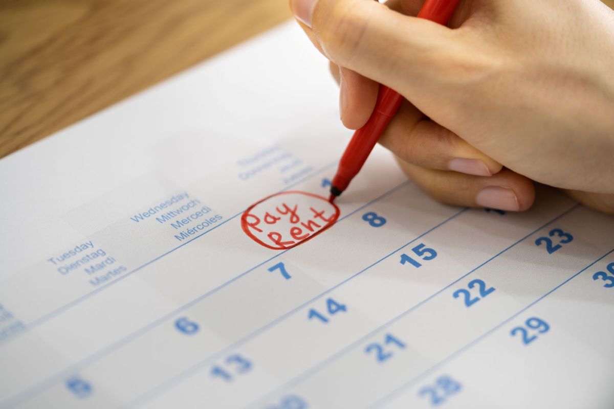 A person writing a "pay rent" note on a calendar.