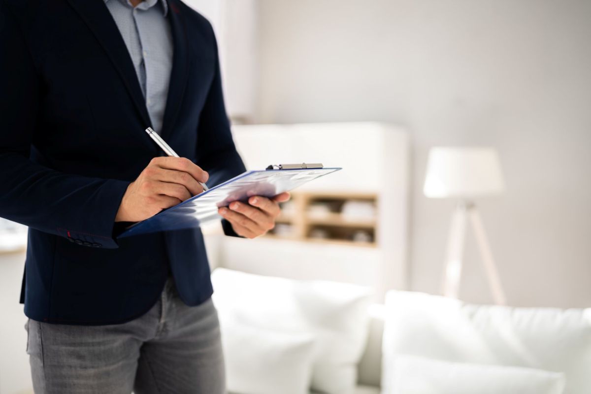 A man wearing a blazer holds a clipboard to inspect the room he's standing in