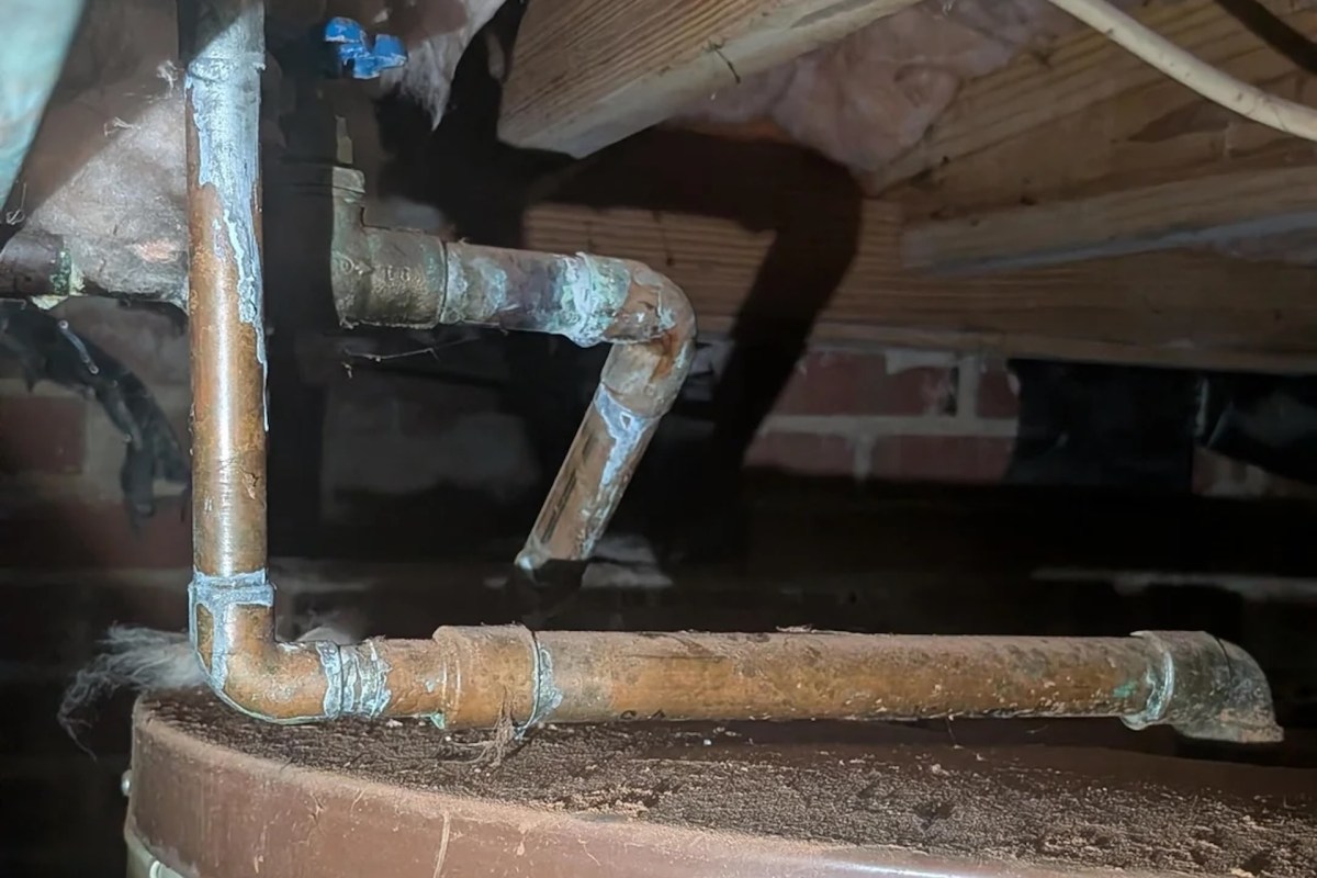 Copper and metal pipes of a hot water heater running along a wooden surface in a dimly lit space.