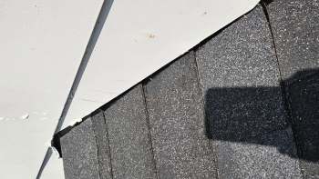 A section of a roof showing black shingles and a nearby white surface.