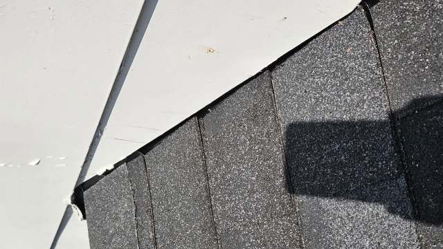 A section of a roof showing black shingles and a nearby white surface.