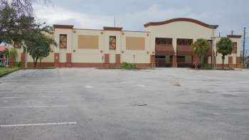 An empty building with a large parking lot and a few trees nearby.