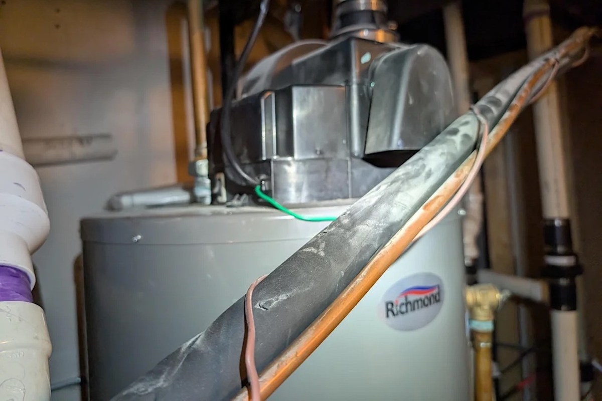A water heater with visible pipes and wires in a utility space.
