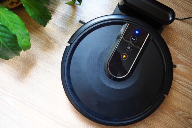 A round robot vacuum sits in a charging station with lights on